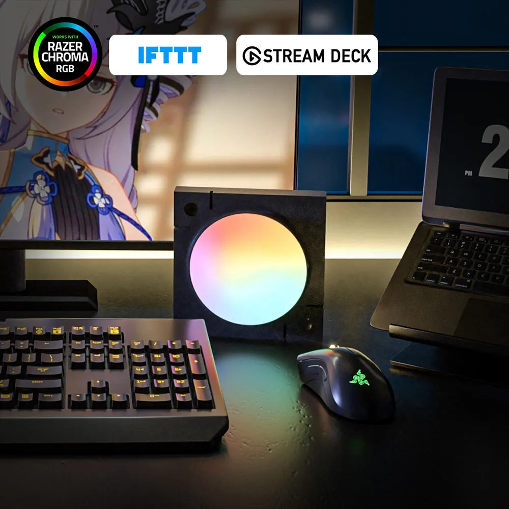A desktop setup featuring a black square IFTTT Stream Deck device with a glowing circular face showing a rainbow gradient, alongside a keyboard, mouse, monitor, and laptop on a dark desk. Promotional badges at the top read 'RAZER CHROMA RGB', 'IFTTT', and 'STREAM DECK'.